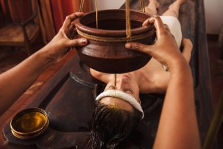 massaggio shirodhara, un filo d'olio cola sulla fronte di una donna supina